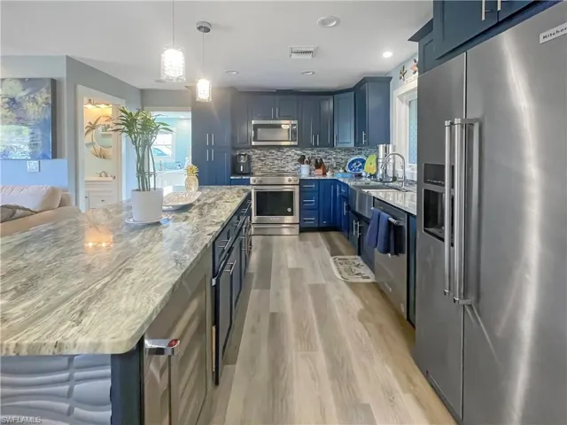Kitchen with stainless steel appliances, light stone counters, blue cabinetry, and light wood finished floors