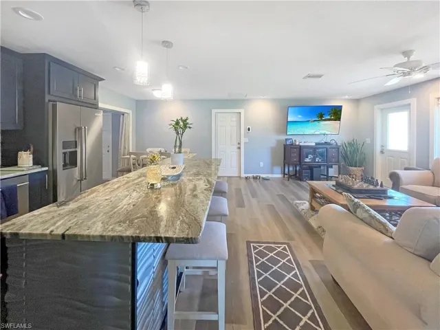Kitchen featuring open floor plan, high end refrigerator, dark wood-style floors, light stone counters, and ceiling fan