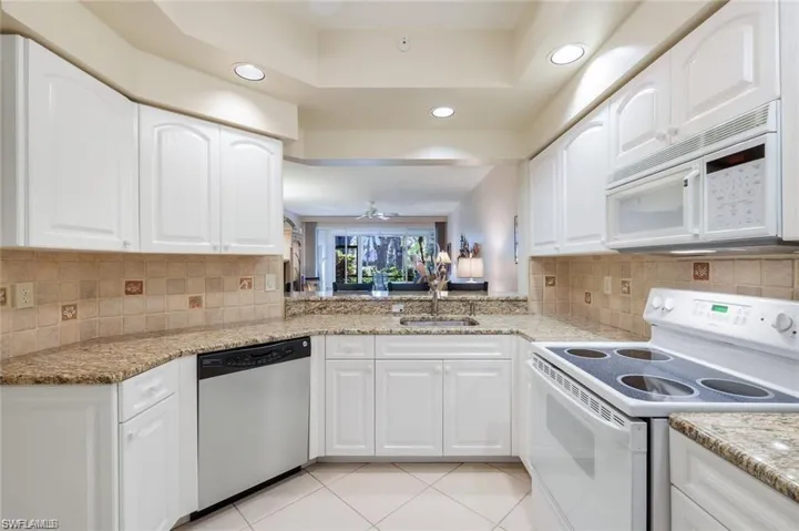 Kitchen with white appliances, white cabinetry, light stone countertops, a tray ceiling, and recessed lighting