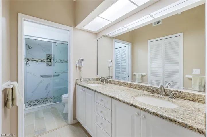 Bathroom featuring double vanity, a marble finish shower, and a closet
