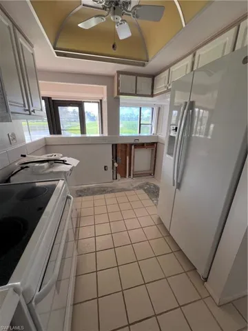 Kitchen with fridge, a raised ceiling, ceiling fan, stove, and tile counters