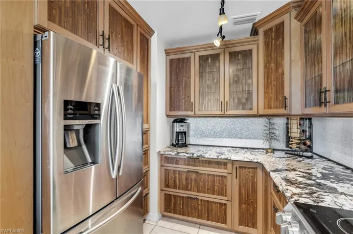 Kitchen featuring light stone countertops, rail lighting, tasteful backsplash, stainless steel fridge with ice dispenser, and light tile patterned flooring