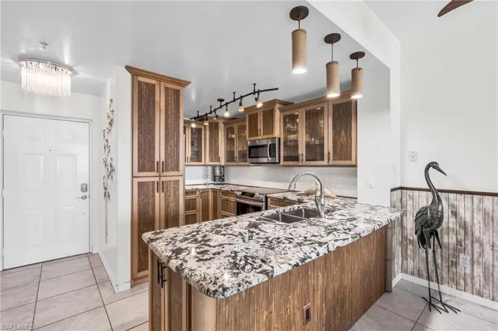 Kitchen with sink, kitchen peninsula, decorative light fixtures, light tile patterned floors, and appliances with stainless steel finishes