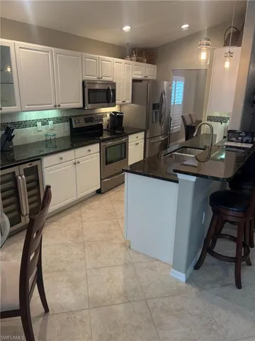 Kitchen with white cabinetry, appliances with stainless steel finishes, dark stone counters, pendant lighting, and decorative backsplash