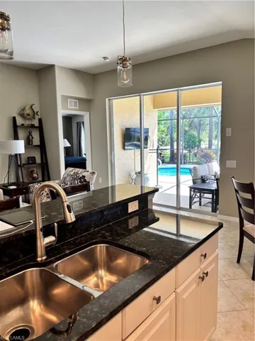 Kitchen with light tile patterned floors, dark stone counters, decorative light fixtures, and white cabinets