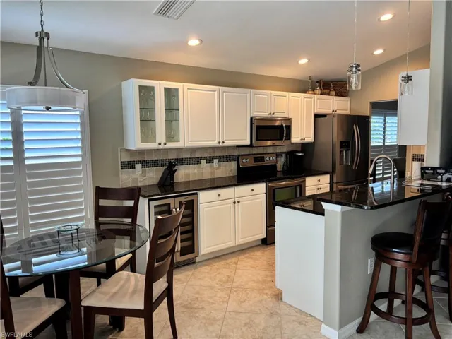 Kitchen featuring wine cooler, appliances with stainless steel finishes, backsplash, dark countertops, and recessed lighting