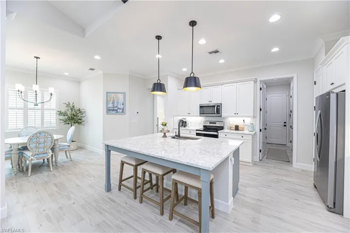 Kitchen with hanging light fixtures, an island with sink, white cabinets, and appliances with stainless steel finishes