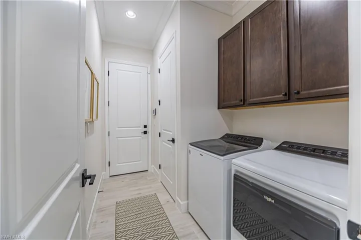 Laundry area featuring crown molding, cabinets, washer and clothes dryer, and light hardwood / wood-style floors