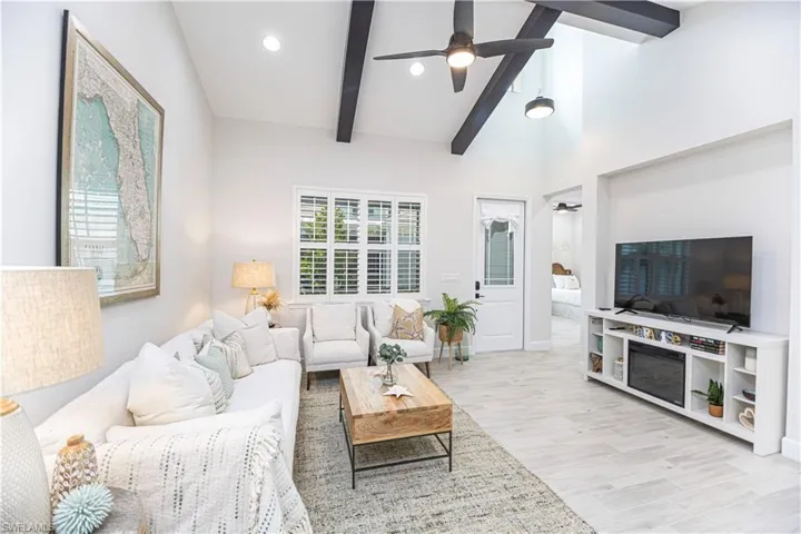 Living room featuring beam ceiling, high vaulted ceiling, ceiling fan, and light wood-type flooring