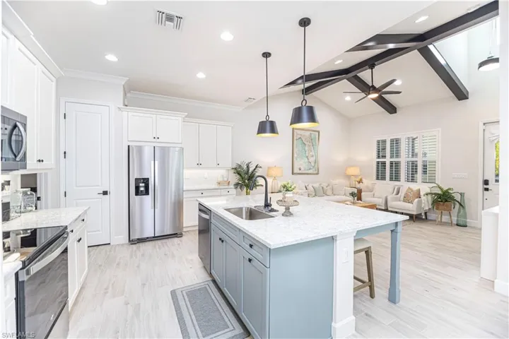 Kitchen featuring sink, pendant lighting, stainless steel appliances, a kitchen island with sink, and white cabinets