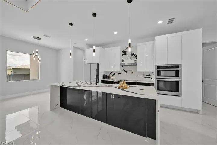 Kitchen with a center island with sink, hanging light fixtures, stainless steel double oven, and wall chimney exhaust hood