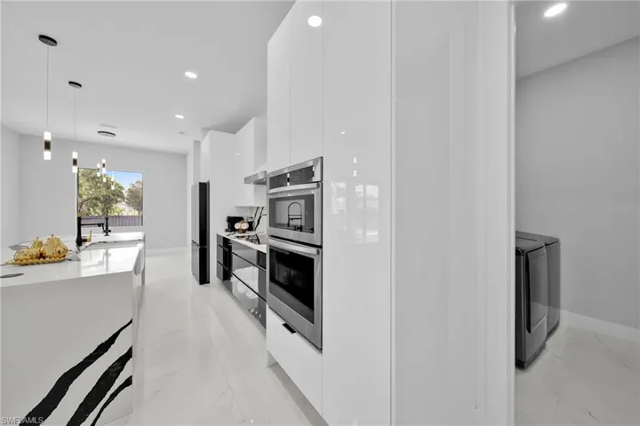 Kitchen with separate washer and dryer, decorative light fixtures, appliances with stainless steel finishes, and white cabinets