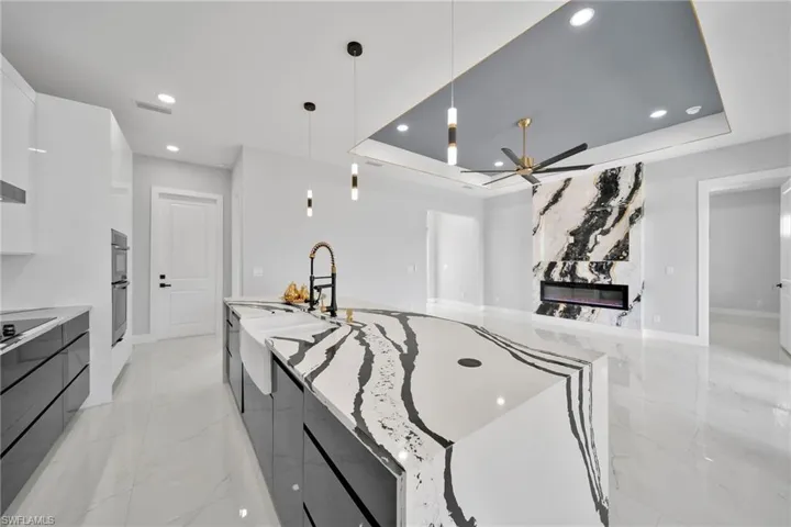 Kitchen with decorative light fixtures, a tray ceiling, stainless steel double oven, ceiling fan, and white cabinets
