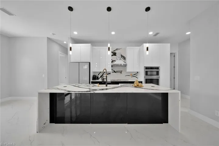 Kitchen featuring pendant lighting, appliances with stainless steel finishes, an island with sink, and custom exhaust hood