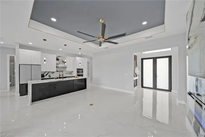 Kitchen with white cabinetry, ceiling fan, a tray ceiling, an island with sink, and pendant lighting