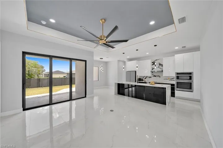 Kitchen with an island with sink, pendant lighting, ceiling fan, and a tray ceiling