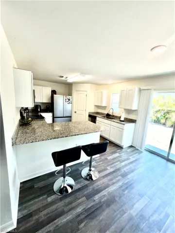 Kitchen featuring granite countertops, white cabinetry, wood-finish flooring, stainless steel appliances, and a sliding glass door
