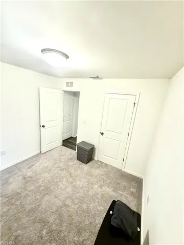 Spacious room featuring light gray carpet flooring, white walls, and a contemporary ceiling light fixture