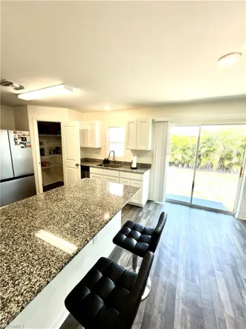 Kitchen featuring a spacious island with a speckled countertop, white cabinetry, and wood-finish flooring