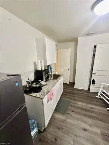 Compact kitchen area featuring white upper and lower cabinetry, a stone-finish countertop, and a stainless steel sink with a tile backsplash
