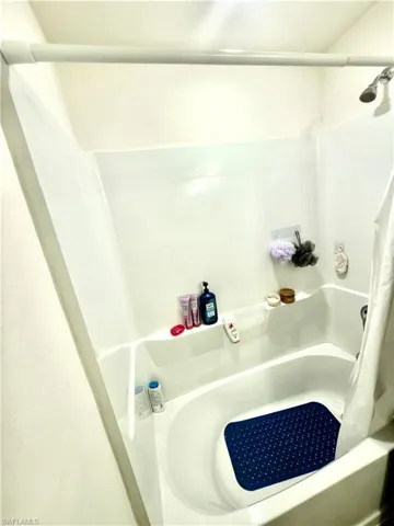 White fiberglass tub and shower combination unit featuring an integrated shelf and showerhead with a chrome finish