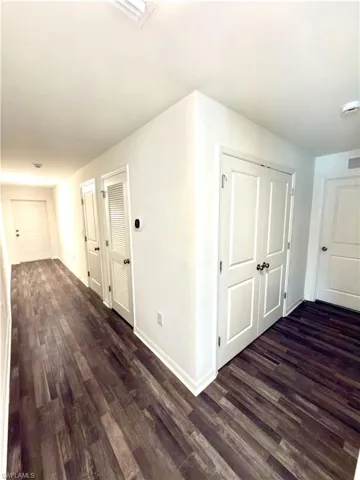 Hallway featuring wood-finish flooring, white baseboards, white walls, and multiple white panel doors