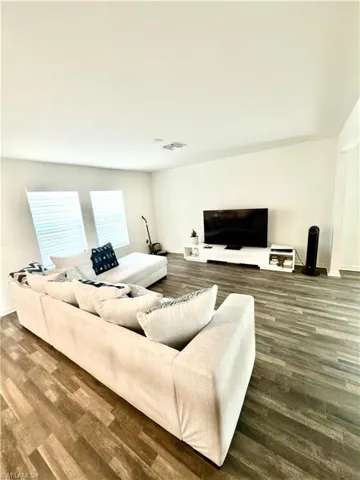 Spacious living area featuring wood-finish flooring, white walls, and abundant natural light from two large windows