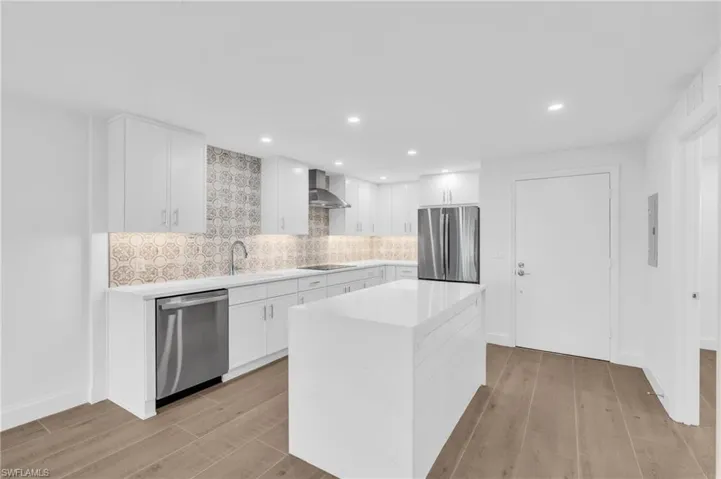 Kitchen with white cabinets, decorative backsplash, light wood-style floors, light stone counters, and stainless steel appliances