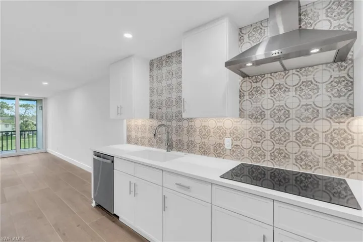Kitchen featuring wall chimney range hood, recessed lighting, white cabinetry, black electric cooktop, and stainless steel dishwasher