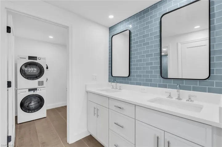 Bathroom with stacked washer / drying machine, double vanity, recessed lighting, decorative backsplash, and light wood-style flooring