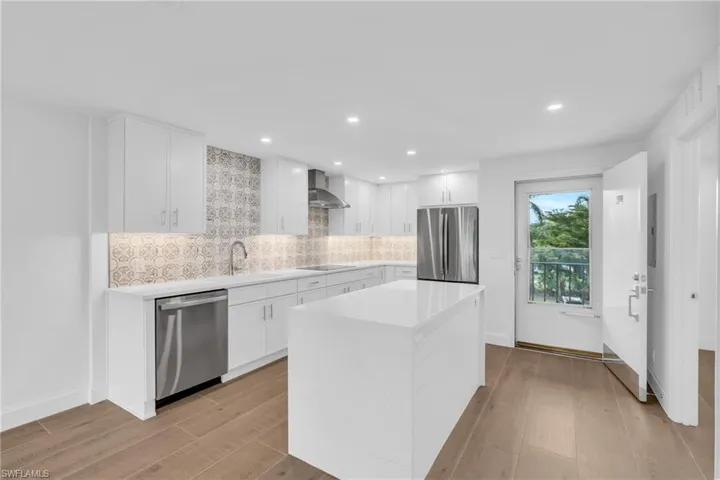 Kitchen featuring white cabinets, decorative backsplash, light wood-type flooring, light stone countertops, and appliances with stainless steel finishes