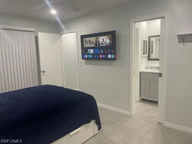 Bedroom with baseboards, ensuite bath, light wood finished floors, and a ceiling fan