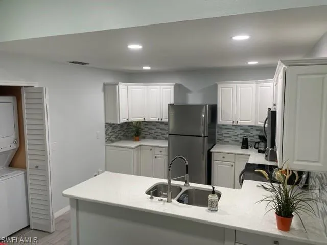 Kitchen featuring stacked washer / drying machine, freestanding refrigerator, a sink, a peninsula, and tasteful backsplash