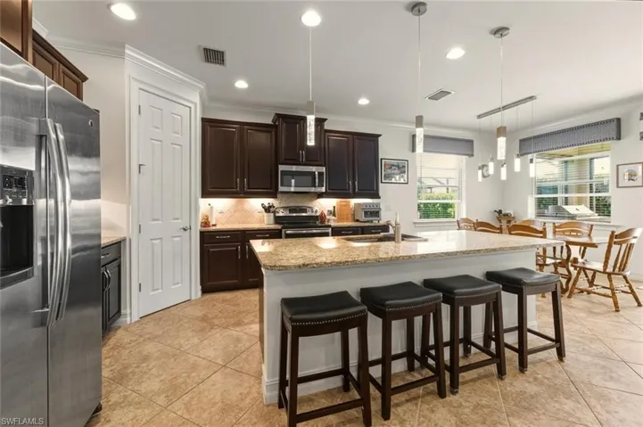 Kitchen with appliances with stainless steel finishes, pendant lighting, light stone countertops, crown molding, and dark brown cabinets