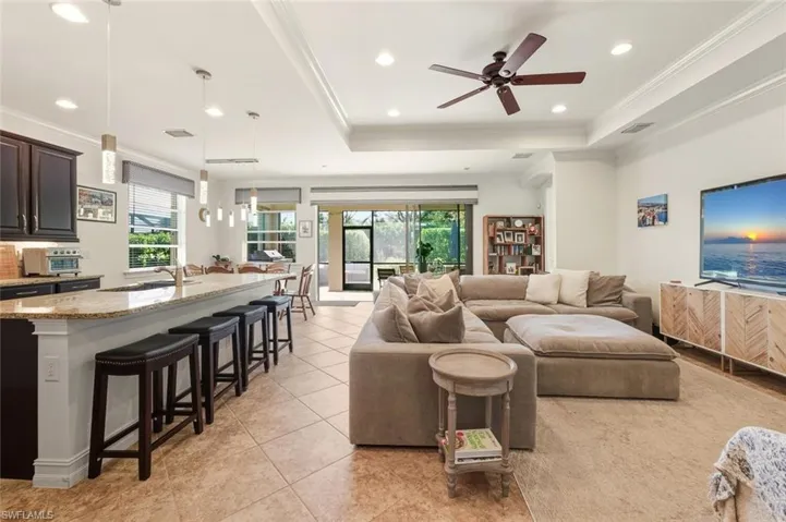 Living room featuring ornamental molding, light tile patterned floors, a raised ceiling, recessed lighting, and ceiling fan