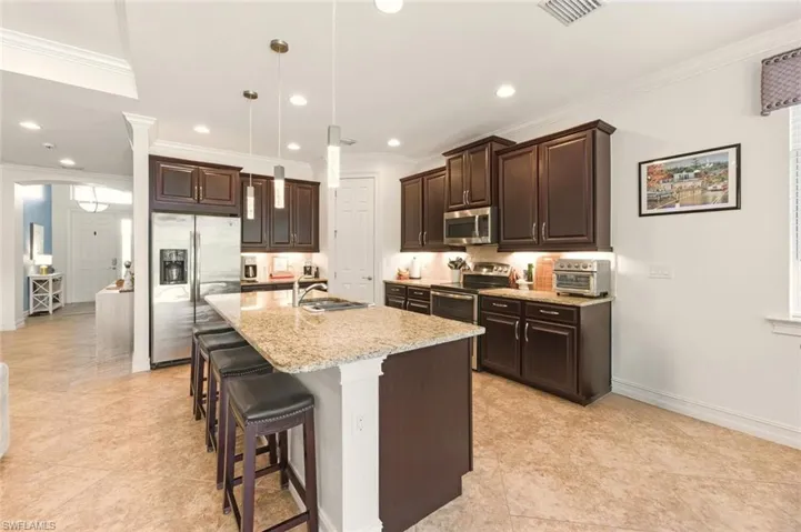 Kitchen with dark brown cabinets, stainless steel appliances, decorative light fixtures, a kitchen breakfast bar, and crown molding