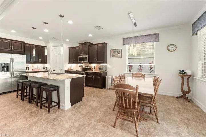 Kitchen featuring dark brown cabinets, crown molding, stainless steel appliances, a breakfast bar, and light stone countertops