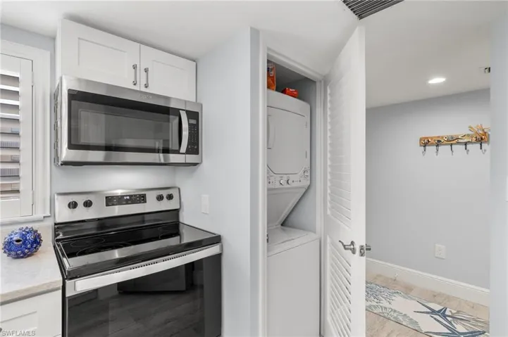 Kitchen with light hardwood / wood-style flooring, appliances with stainless steel finishes, stacked washing maching and dryer, and white cabinetry