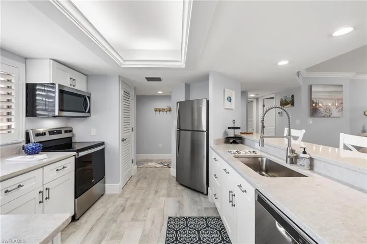 Kitchen featuring stainless steel appliances, light stone countertops, sink, white cabinetry, and light hardwood / wood-style flooring