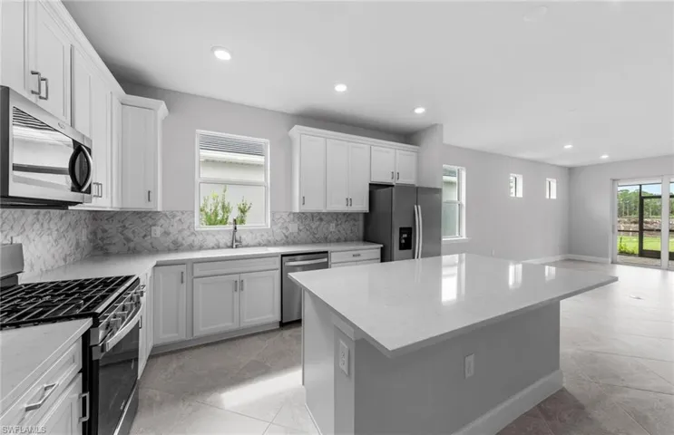 Kitchen with white cabinetry, backsplash, a kitchen island, stainless steel appliances, and sink