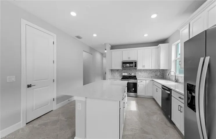 Kitchen featuring a center island, sink, white cabinets, decorative backsplash, and stainless steel appliances