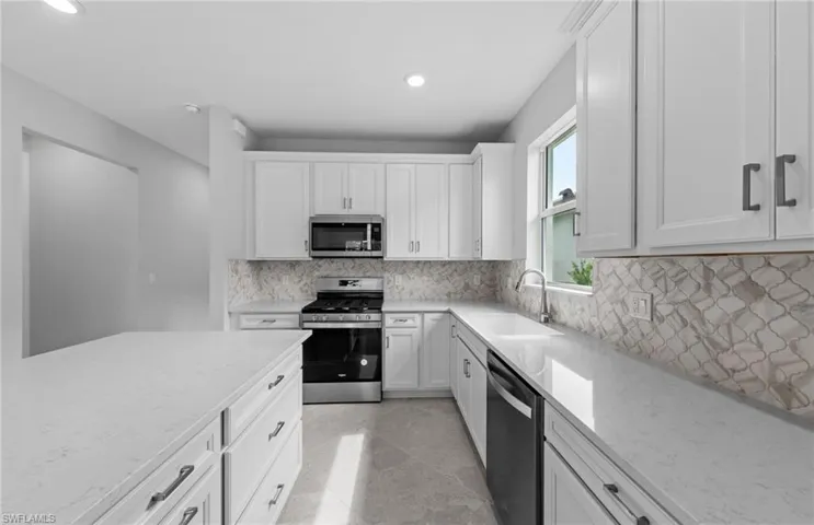 Kitchen featuring appliances with stainless steel finishes, light stone counters, and white cabinets
