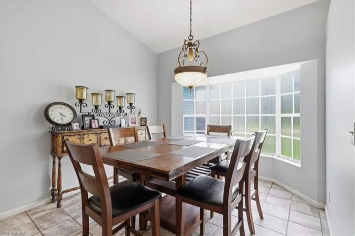 Vaulted ceiling dining area featuring a prominent bay window, overhead chandelier, and tile flooring
