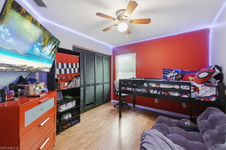 Room featuring wood-finish flooring, a ceiling fan with integrated lighting, and a window with horizontal blinds