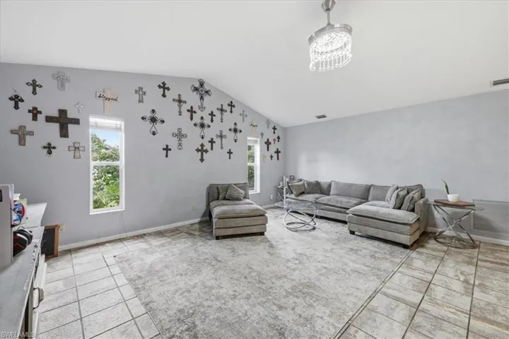 Spacious living area featuring vaulted ceilings, light tile flooring, and a crystal chandelier fixture