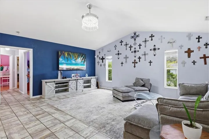 Vaulted ceilings highlight this expansive living area, featuring a decorative chandelier and a prominent accent wall