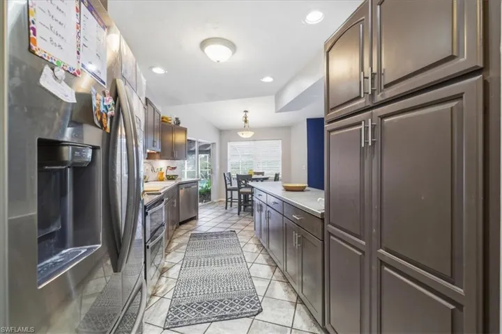 Galley kitchen featuring stainless steel appliances, dark wood-finish cabinetry, light-toned countertops, and tile flooring