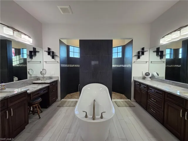 Bathroom featuring a walk in shower, a freestanding bath, healthy amount of natural light, and two vanities