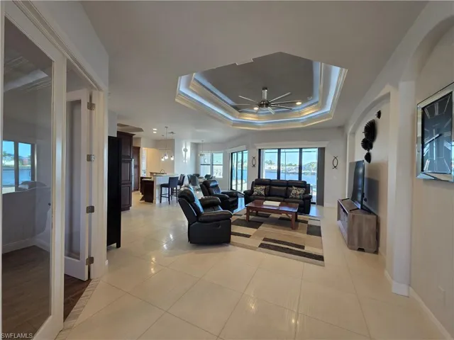 Living room featuring ceiling fan, ornamental molding, light tile patterned floors, and a raised ceiling