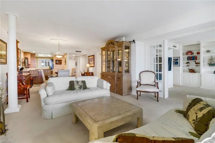 Living room with built in features, light carpet, and ornate columns